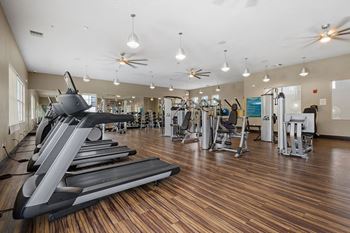 A gym with cardio equipment and weights on a wooden floor